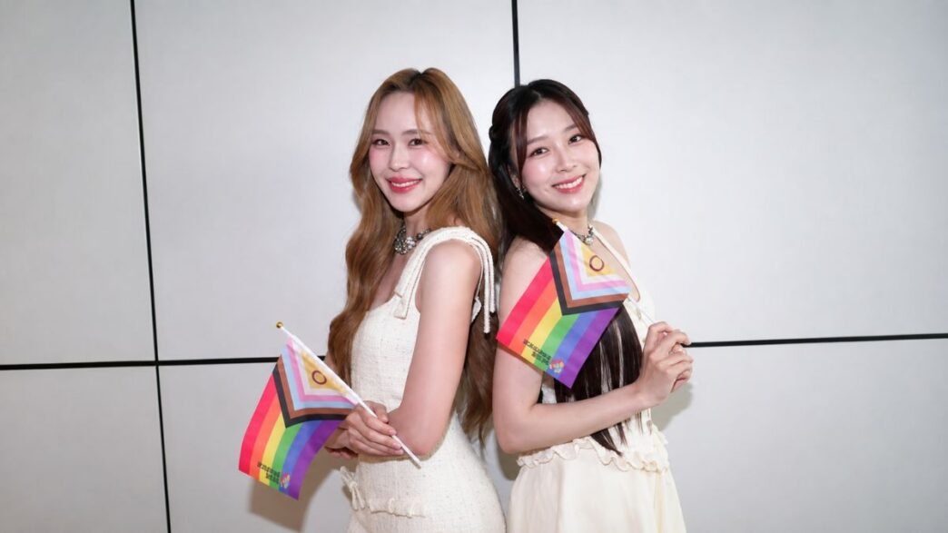 June e Mewnich, protagonistas de Whale Store xoxo, posam juntas segurando bandeiras do orgulho LGBTQIA+