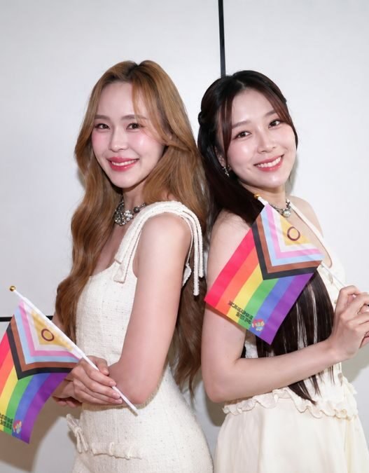 June e Mewnich, protagonistas de Whale Store xoxo, posam juntas segurando bandeiras do orgulho LGBTQIA+
